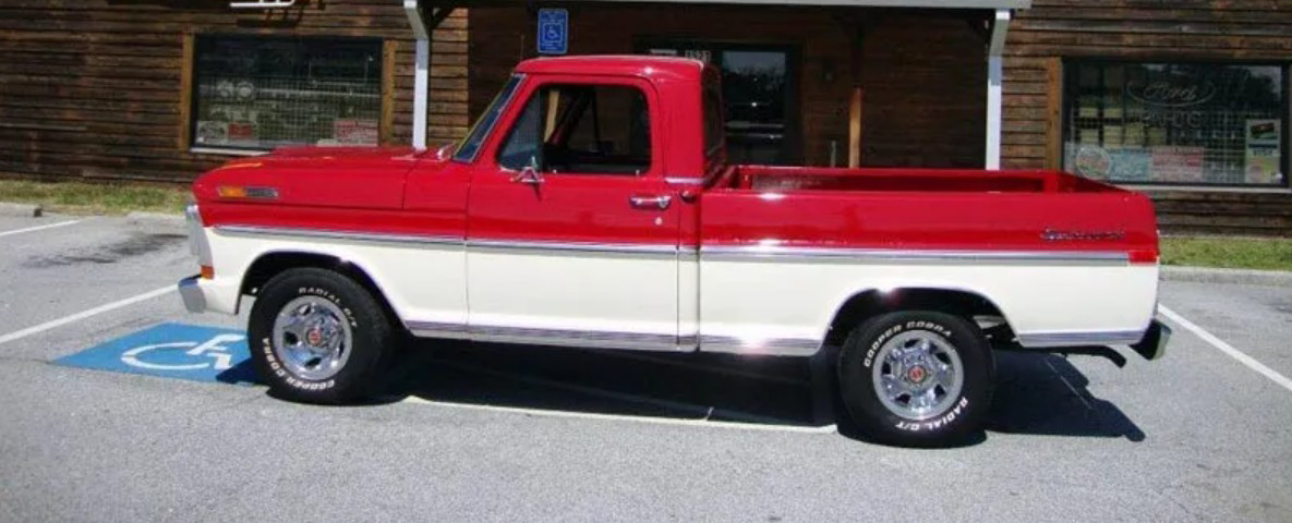 Red and white vintage Ford
 pickup truck parked in a handicapped parking space