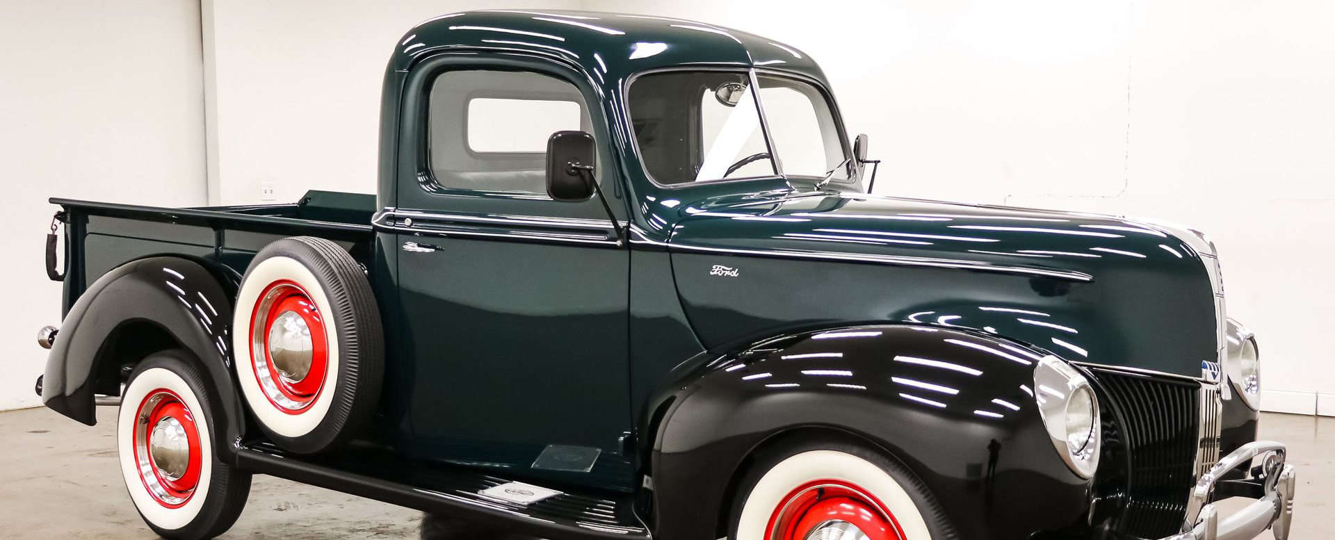 Dark green vintage Ford 
pickup truck with whitewall tires on a white background