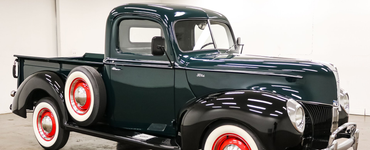 Dark green vintage Ford 
pickup truck with whitewall tires on a white background