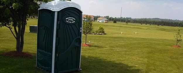 a green portable toilet set up in a wide green field