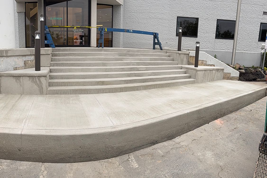 Concrete steps and ramp leading to a building entrance with blue handrails and stone walls