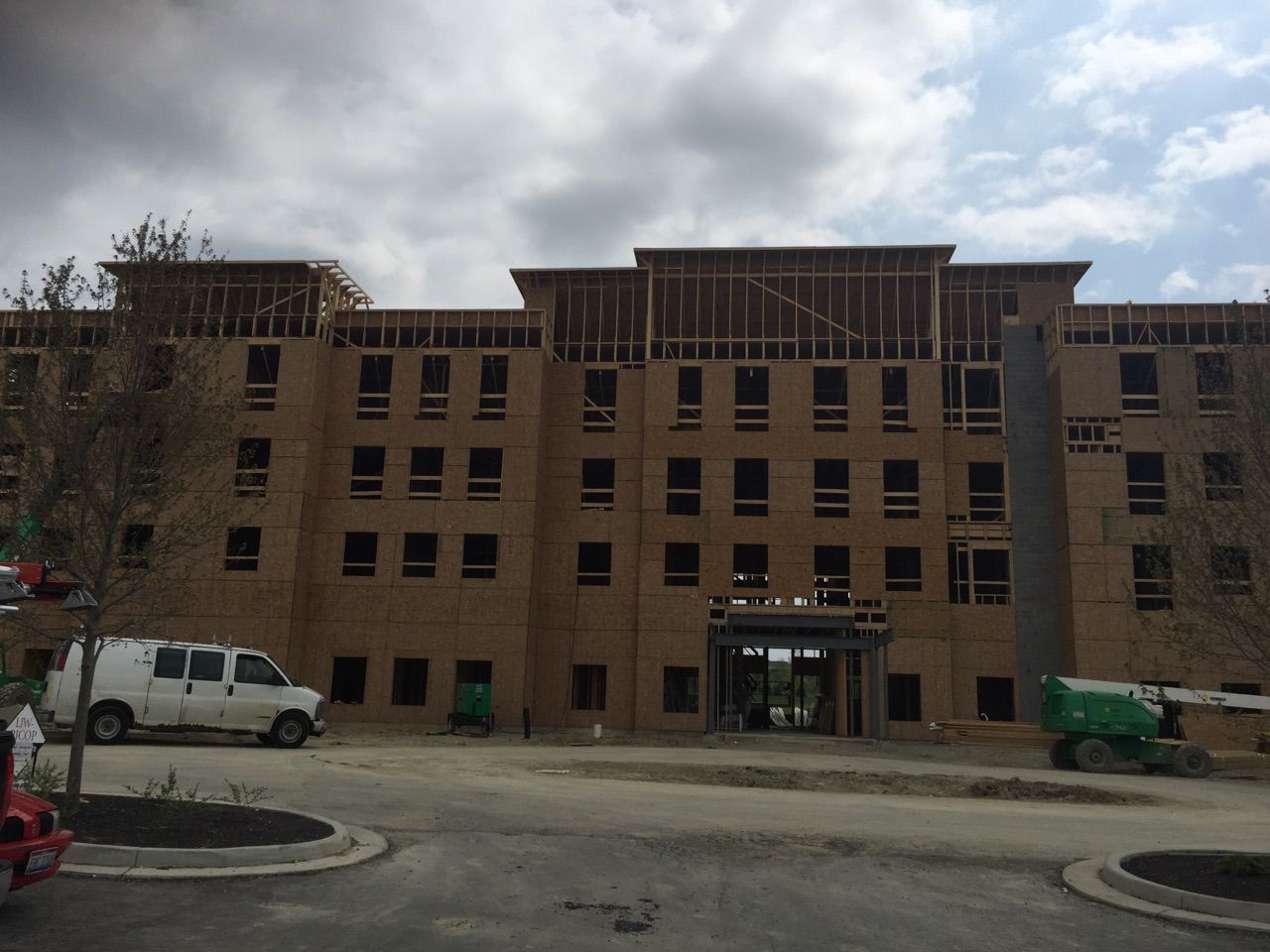 A multistory apartment building under construction with exposed wooden framing and a large crane on a cloudy day.