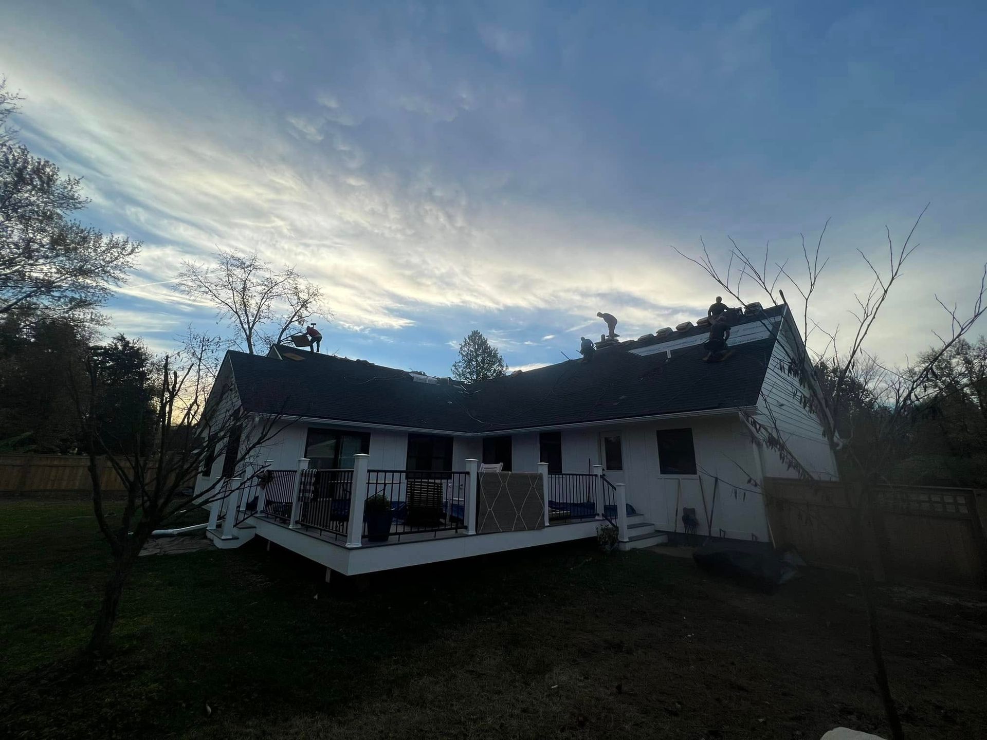 Workers on the roof of a white, L-shaped house with a wooden deck during the golden hour.