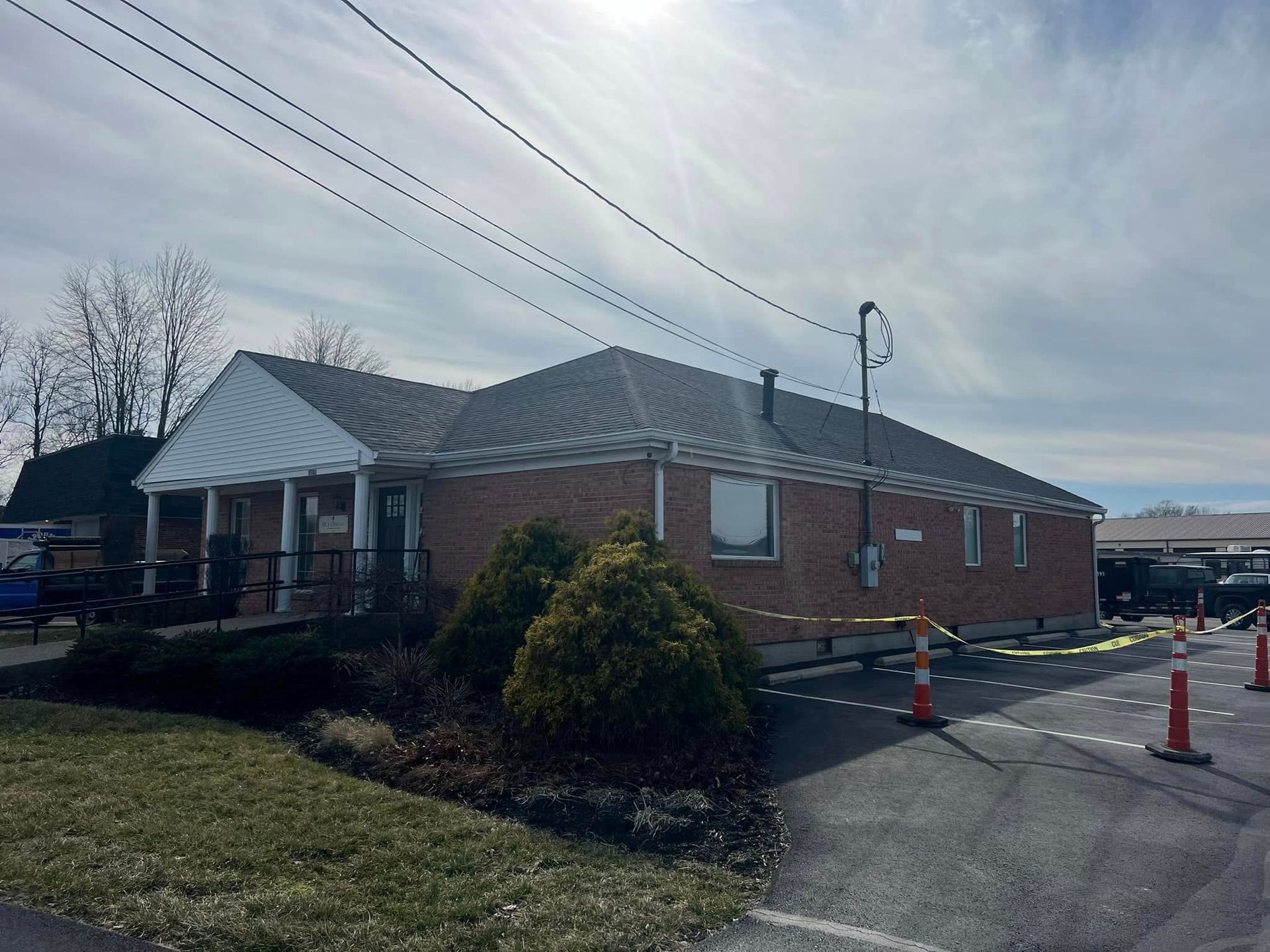 A single-story brick building with a white gabled entrance, surrounded by parking spots marked with orange safety cones.