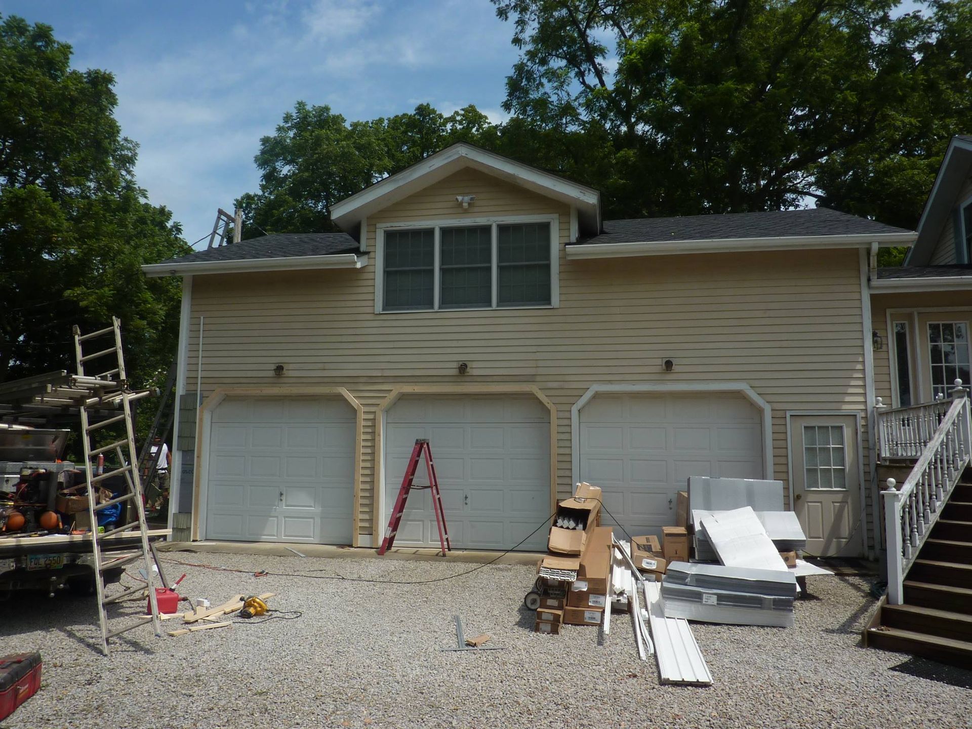 A beige three-car garage under construction with a ladder and building supplies scattered on the gravel driveway.