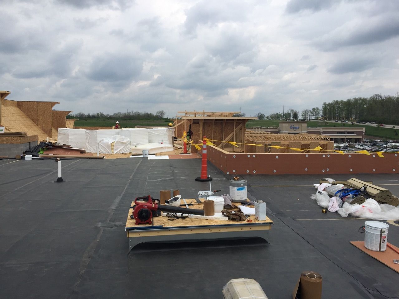 A rooftop construction site with materials, tools on a wooden platform, and unfinished wooden structures under cloudy skies.