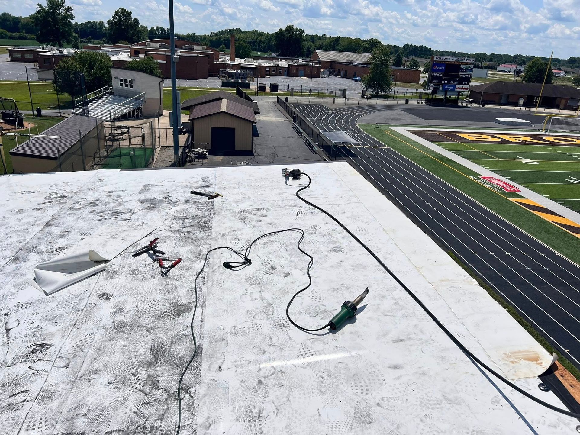 A white-roofed building overlooking a high school football field and running track on a sunny day.