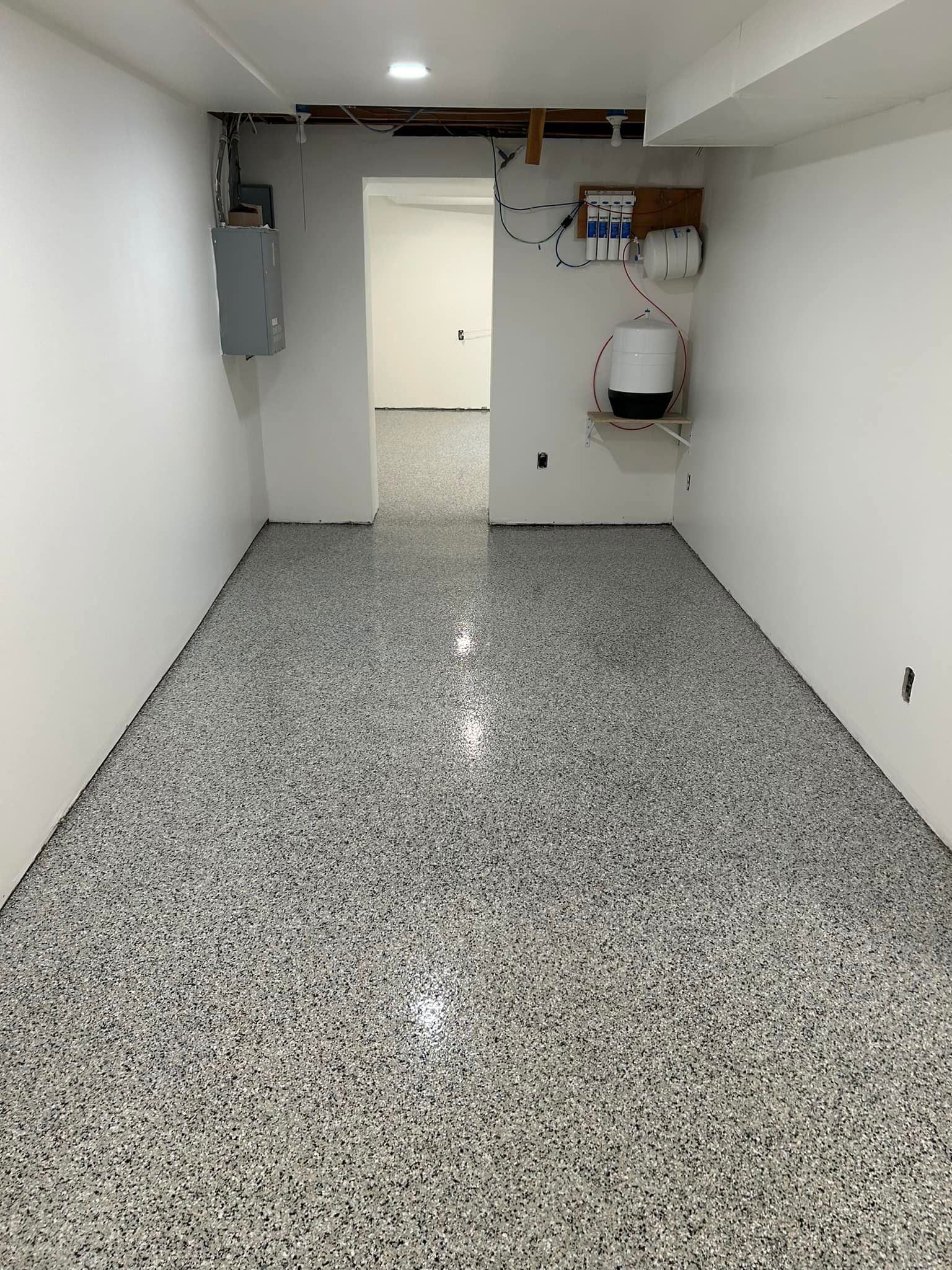 Room with speckled gray flooring and white walls. Doorway leads to another room.
