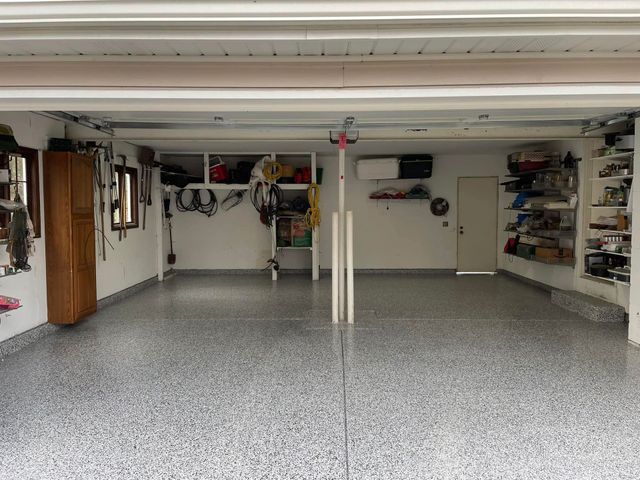 Garage interior with epoxy floor, shelves, storage cabinets, and open door.