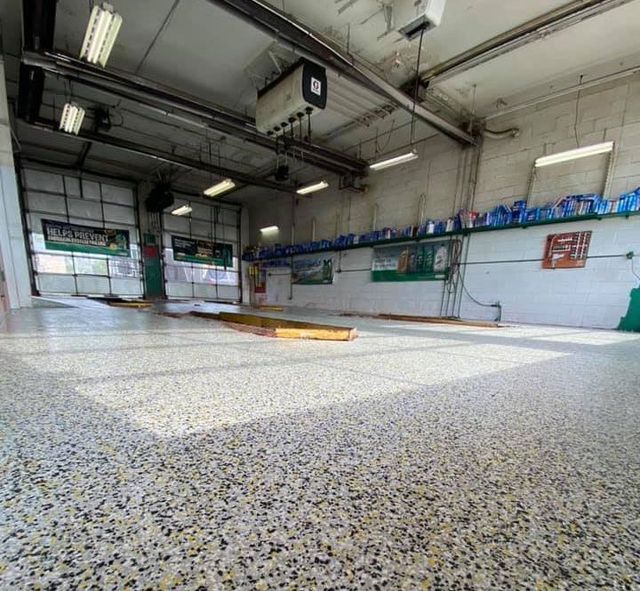 Garage interior with a speckled floor, open doors, and overhead lights.