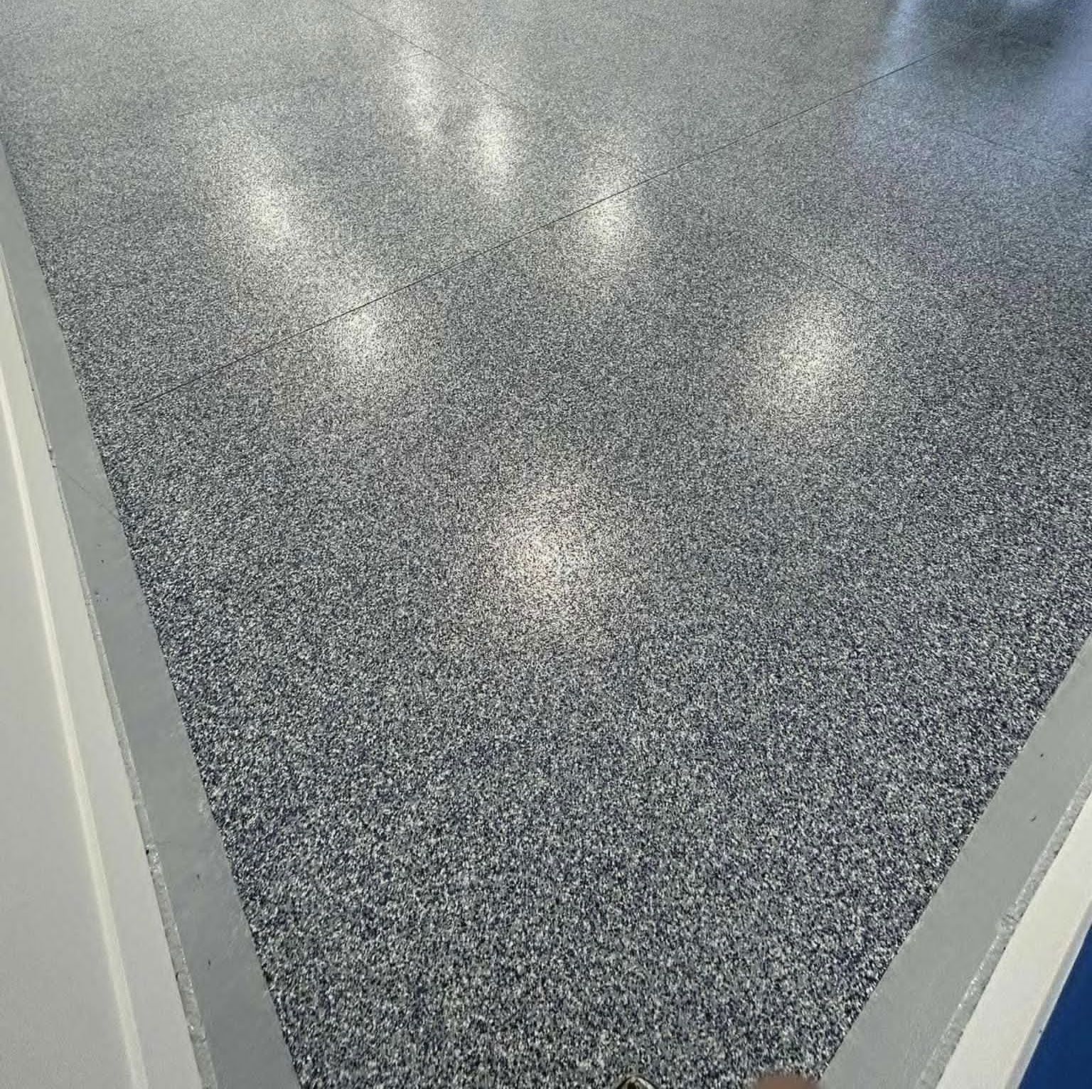 Epoxy floor with speckled gray and white chips, reflecting bright overhead lights.