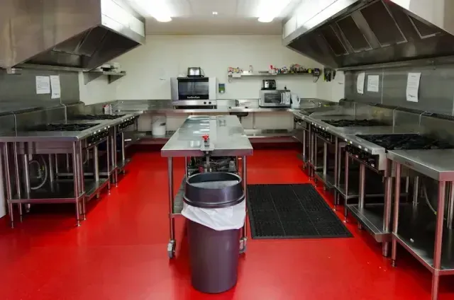 Commercial kitchen with stainless steel counters, stoves, and a red floor.