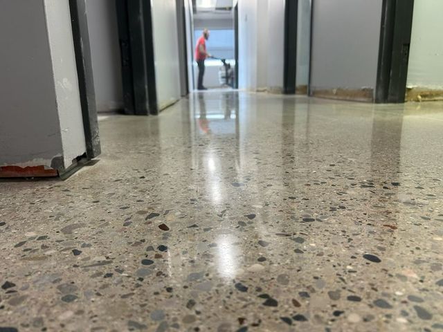 Polished concrete floor in a hallway, reflecting light. A person stands in the background.