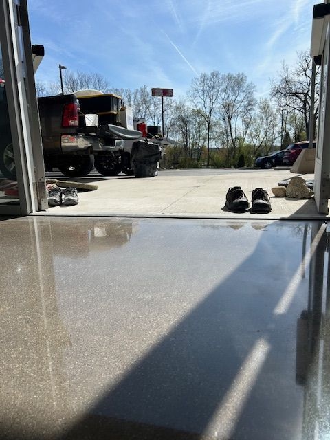 View from inside, looking out at a vehicle, trees, and blue sky. Two pairs of shoes sit on the ground near the exit.