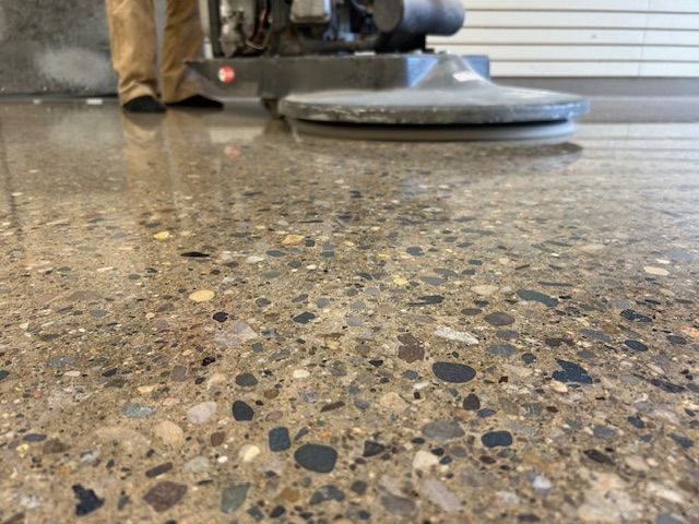 Person polishing a concrete floor with visible aggregate. Machine in use, interior setting.