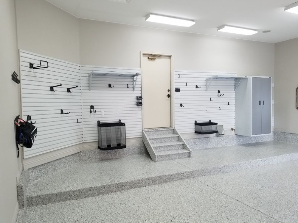 A clean garage with wall storage, gray floor, door, and a gray storage cabinet.