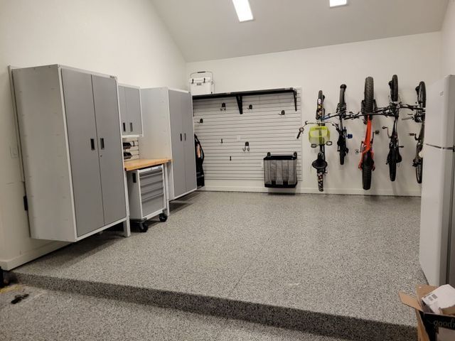 Garage with gray cabinets, tool cabinet, bikes on the wall, and speckled flooring.