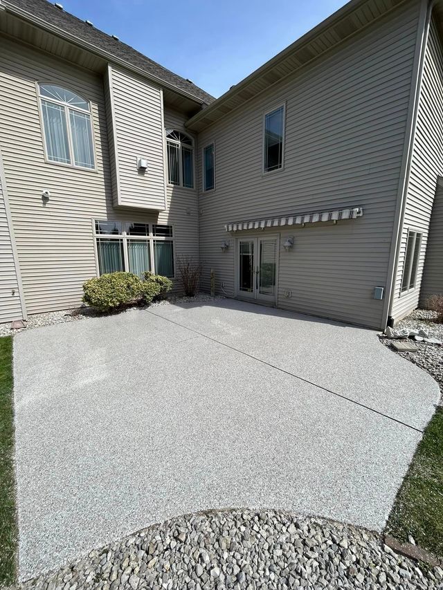 Concrete patio next to a beige house, with rocks on the ground and grass.