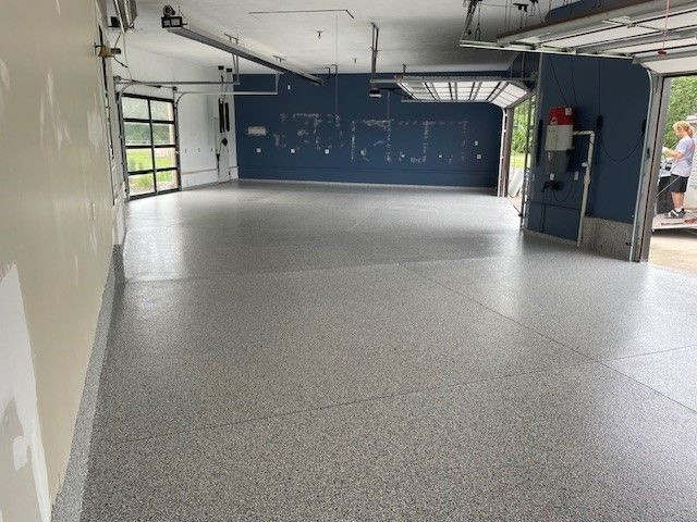 A garage with a gray epoxy floor, blue accent wall, and a person standing in the open doorway.