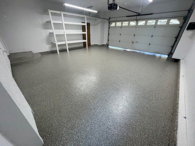Garage with epoxy floor and white shelves, garage door partially open.