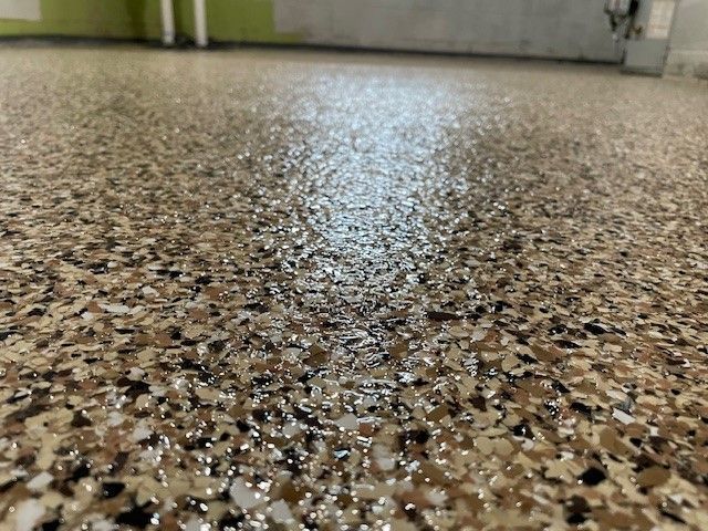 Close-up of a mottled, speckled epoxy floor in shades of tan, brown, and white, reflecting light.