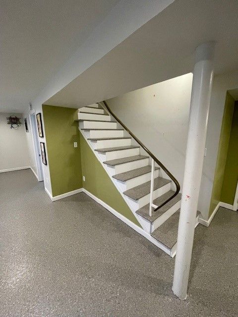 Staircase leading up, with gray steps, white trim, and a green wall, in a room with a speckled gray floor.