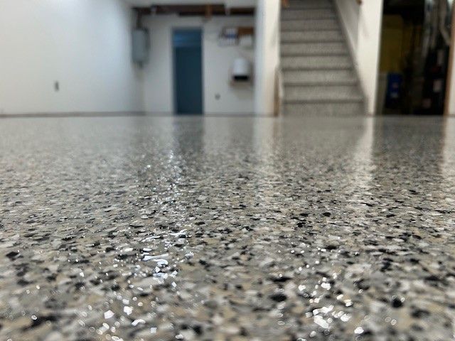Close-up of a shiny, speckled epoxy garage floor, stairs in background.