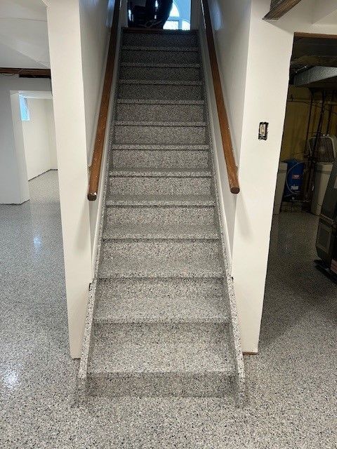 Staircase with gray speckled steps, wooden handrails, and white walls, leading upwards.
