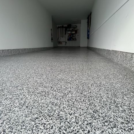 Garage with gray and white speckled epoxy floor, white walls, and tools hanging.