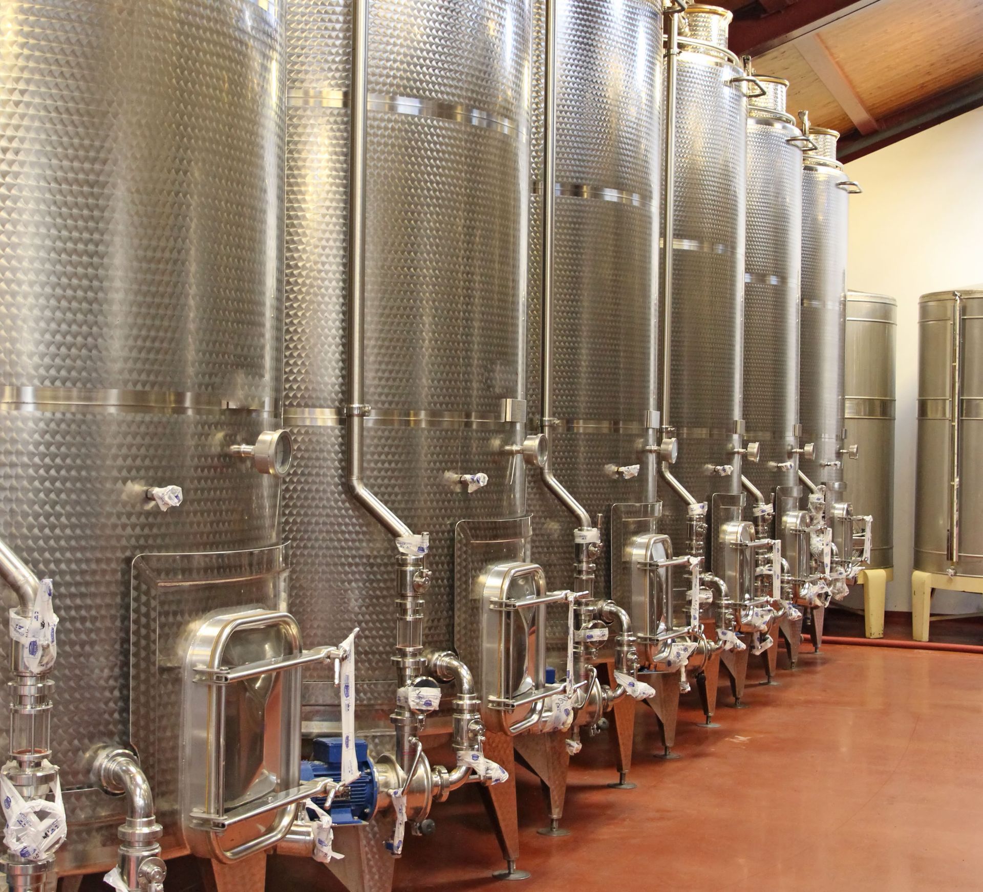 Stainless steel wine fermentation tanks in a winery, lined up in a row.
