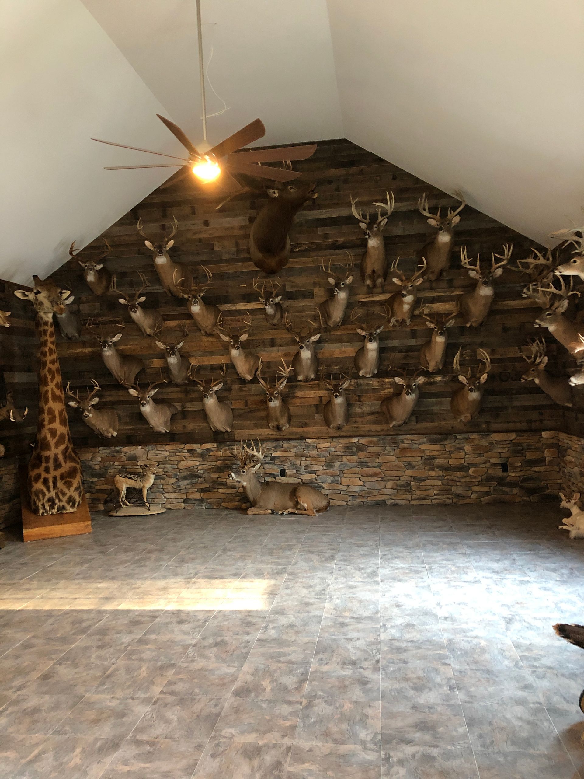 Rustic room with a stone wall, decorative wood pieces, and a ceiling fan under a sloped ceiling.