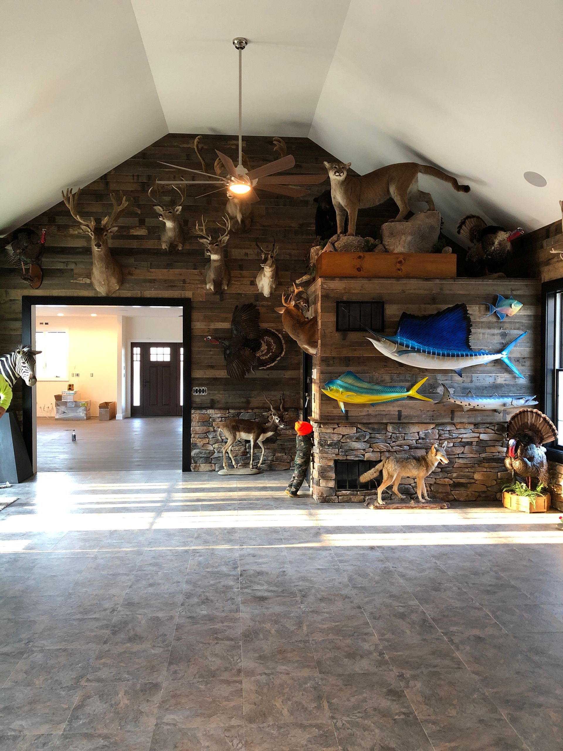 Rustic room with stone wall, mounted fish decor, and sunlight across a gray floor