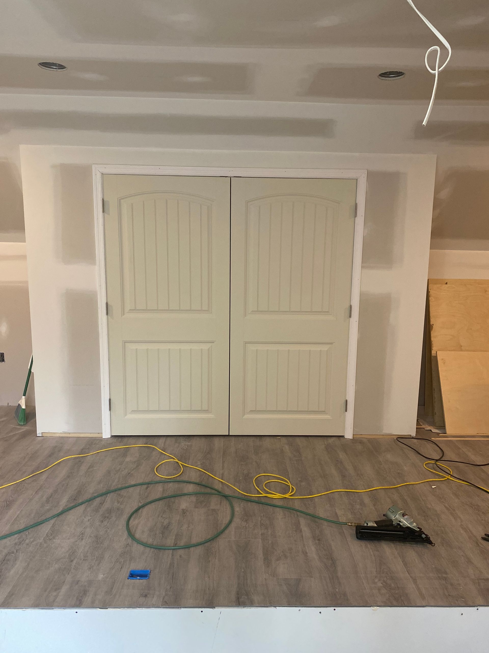 Unfinished room with white double closet doors, drywall patches, and tools on the floor during renovation