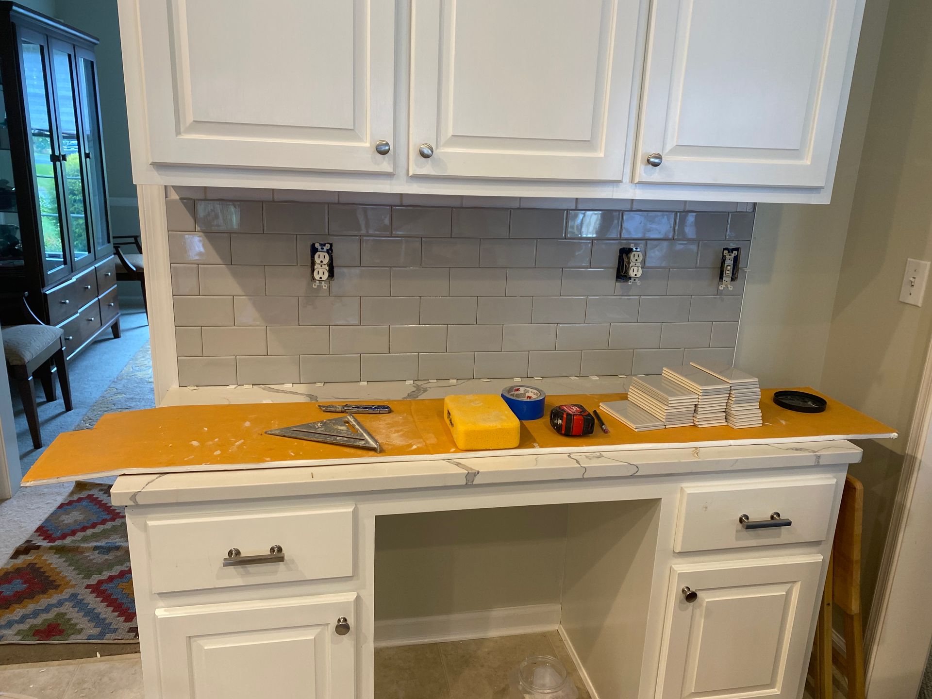 Kitchen counter covered with tools, paint tray, and supplies beneath white cabinets