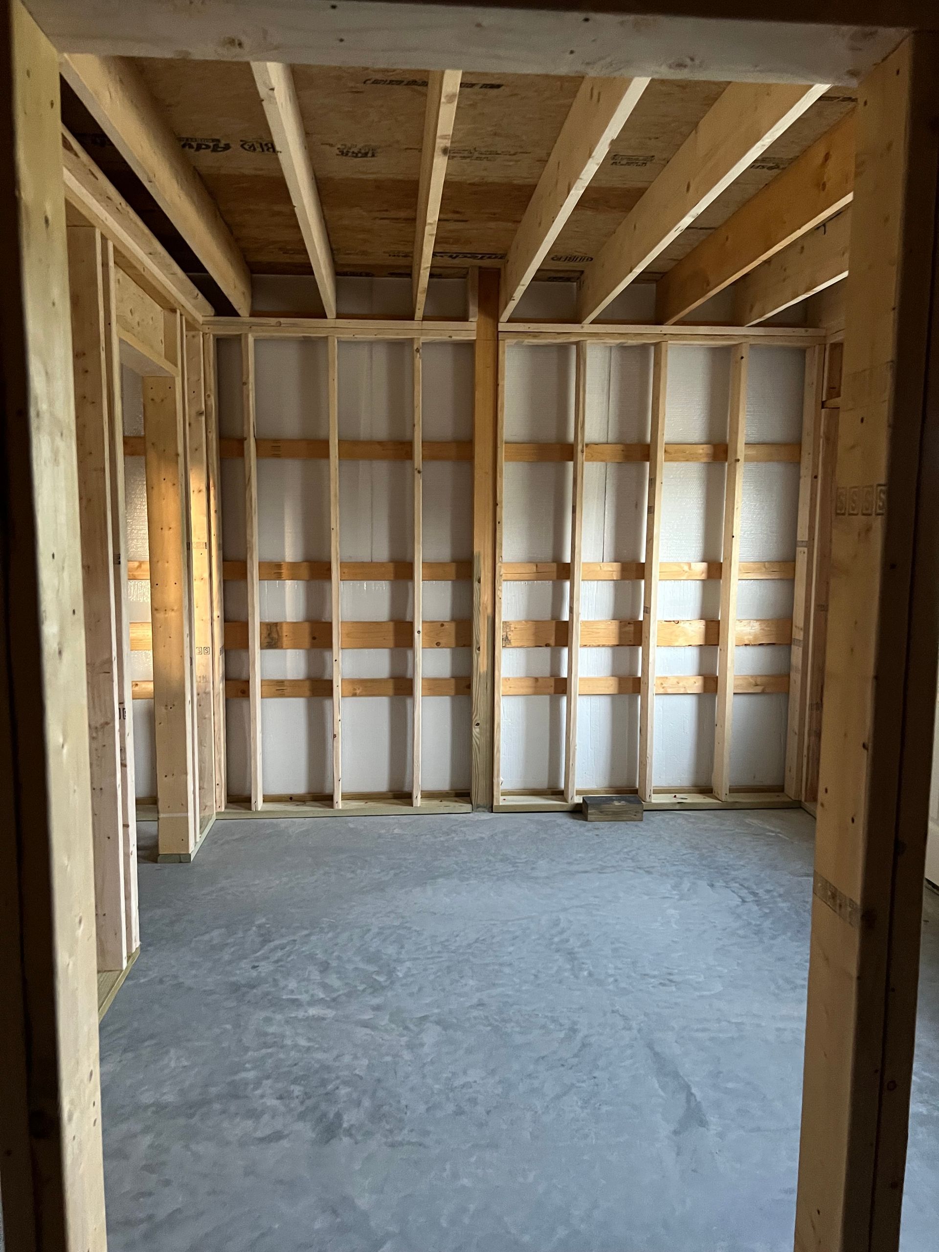 Unfinished wooden room interior with exposed studs, beams, and a concrete floor.