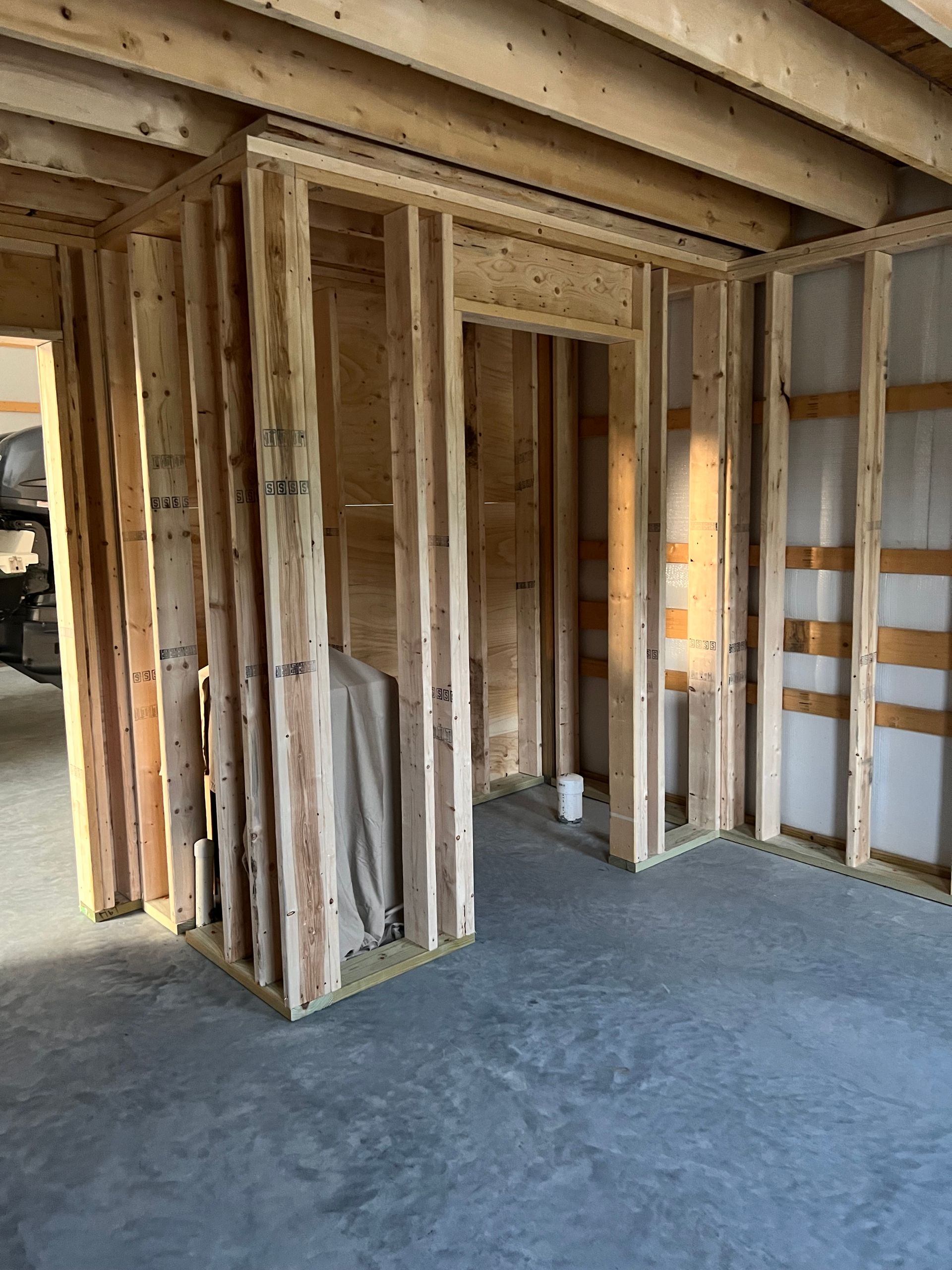 Framed interior of a house under construction with exposed studs and unfinished concrete floor