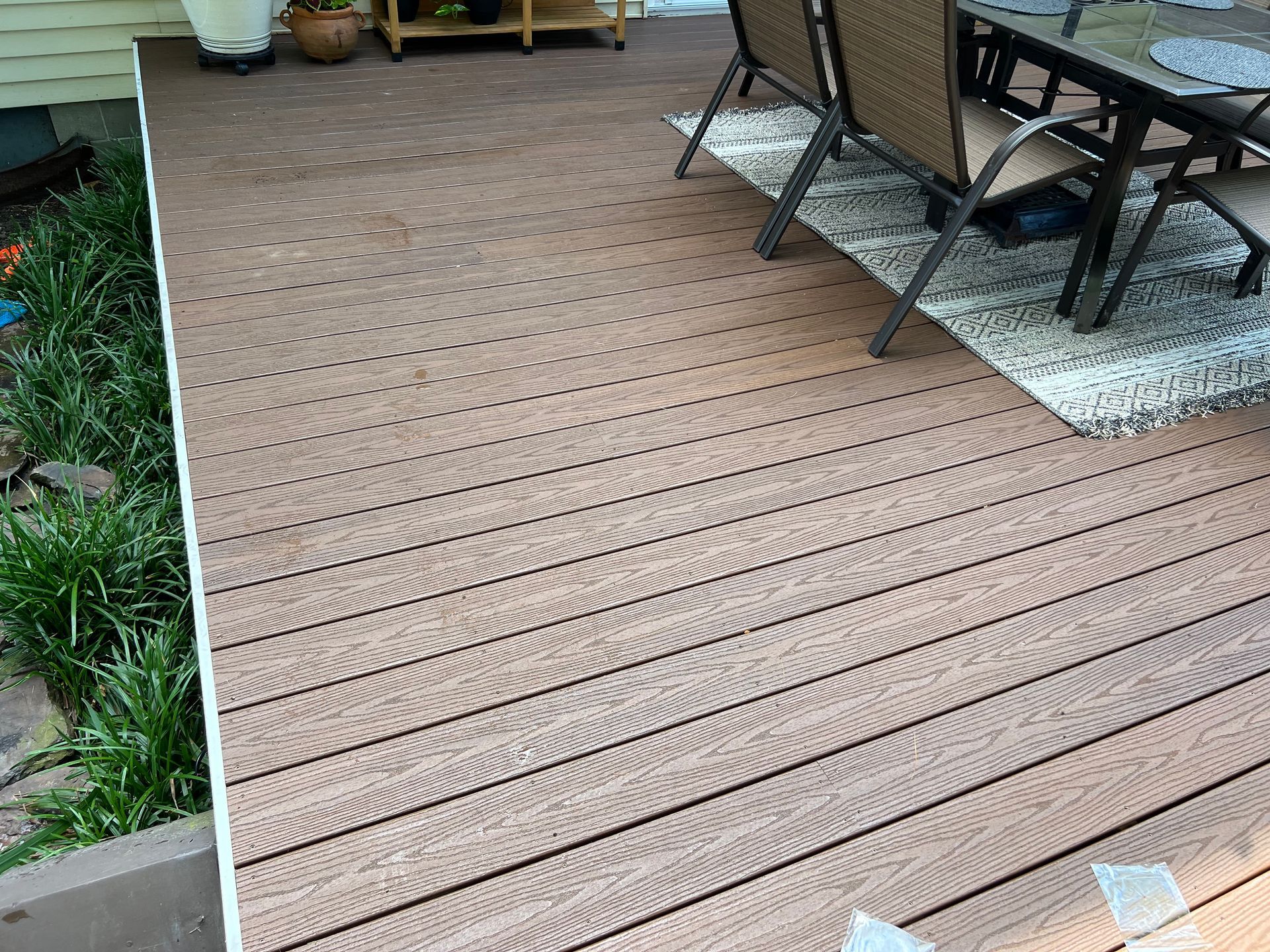 Wooden deck walkway beside a garden, with patio chairs and table on the right.