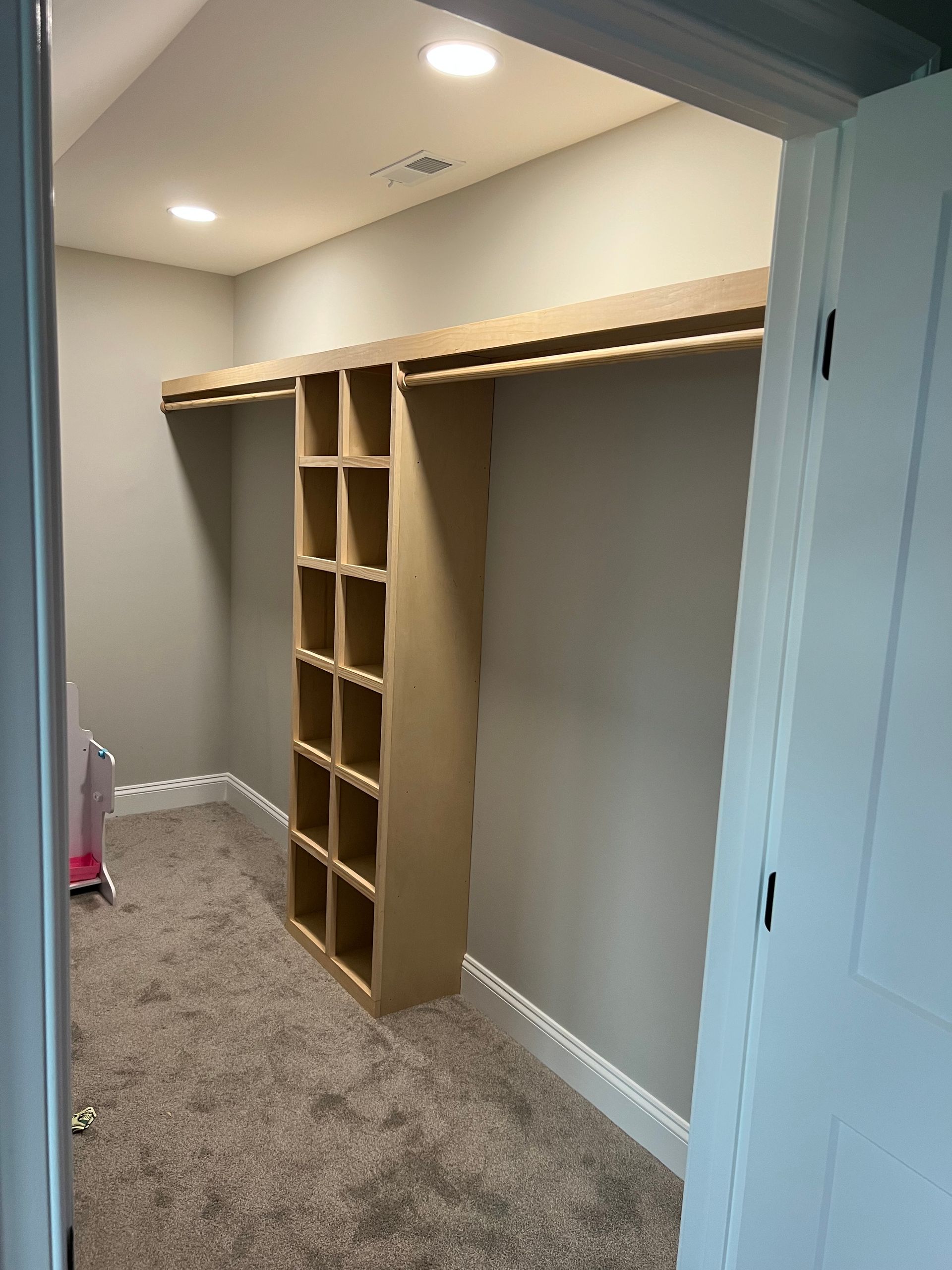 Empty closet with built-in wooden shelving and hanging rods in a carpeted room.