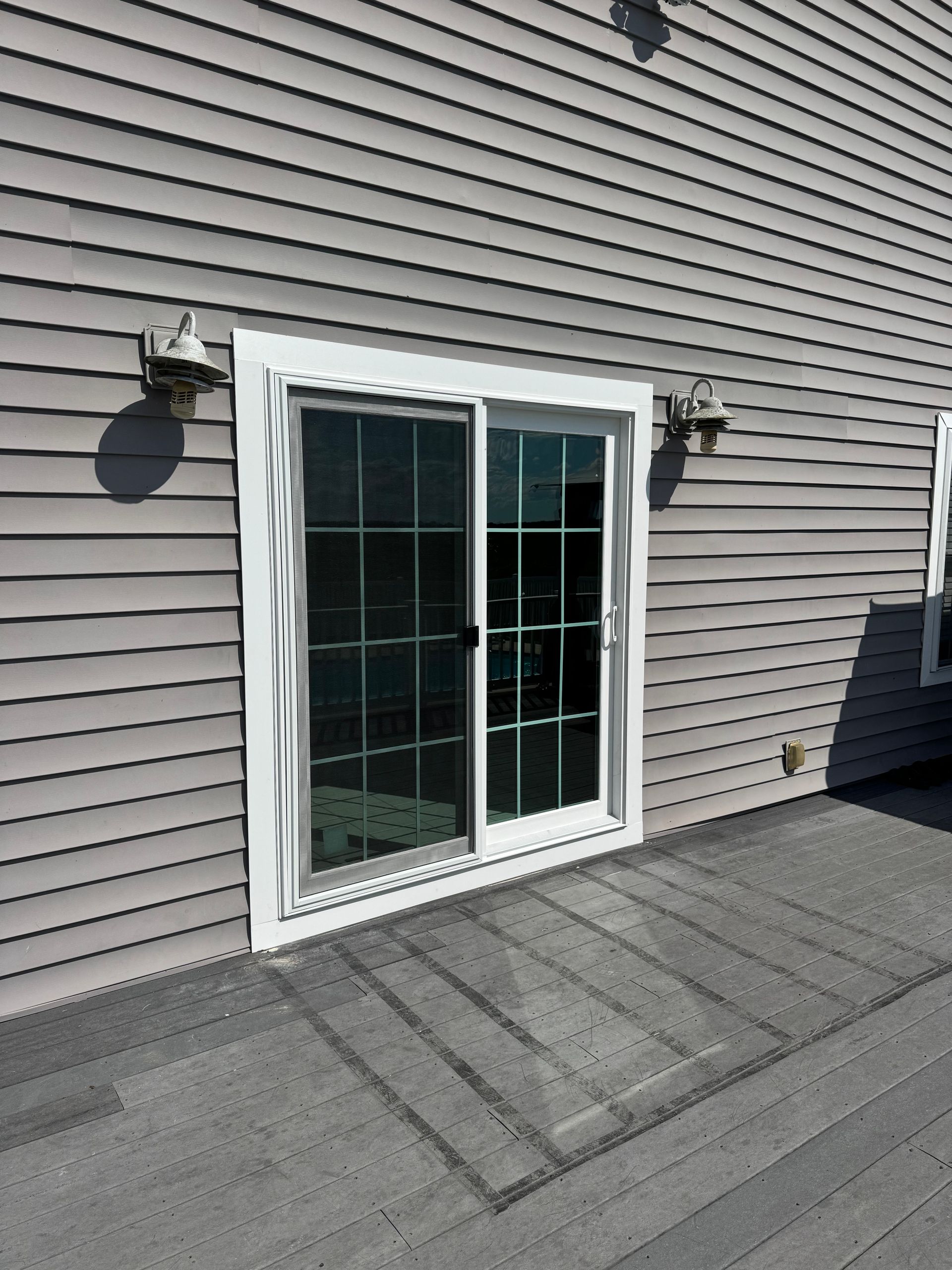 White-framed sliding glass door with blinds on a gray-sided house above a deck.
