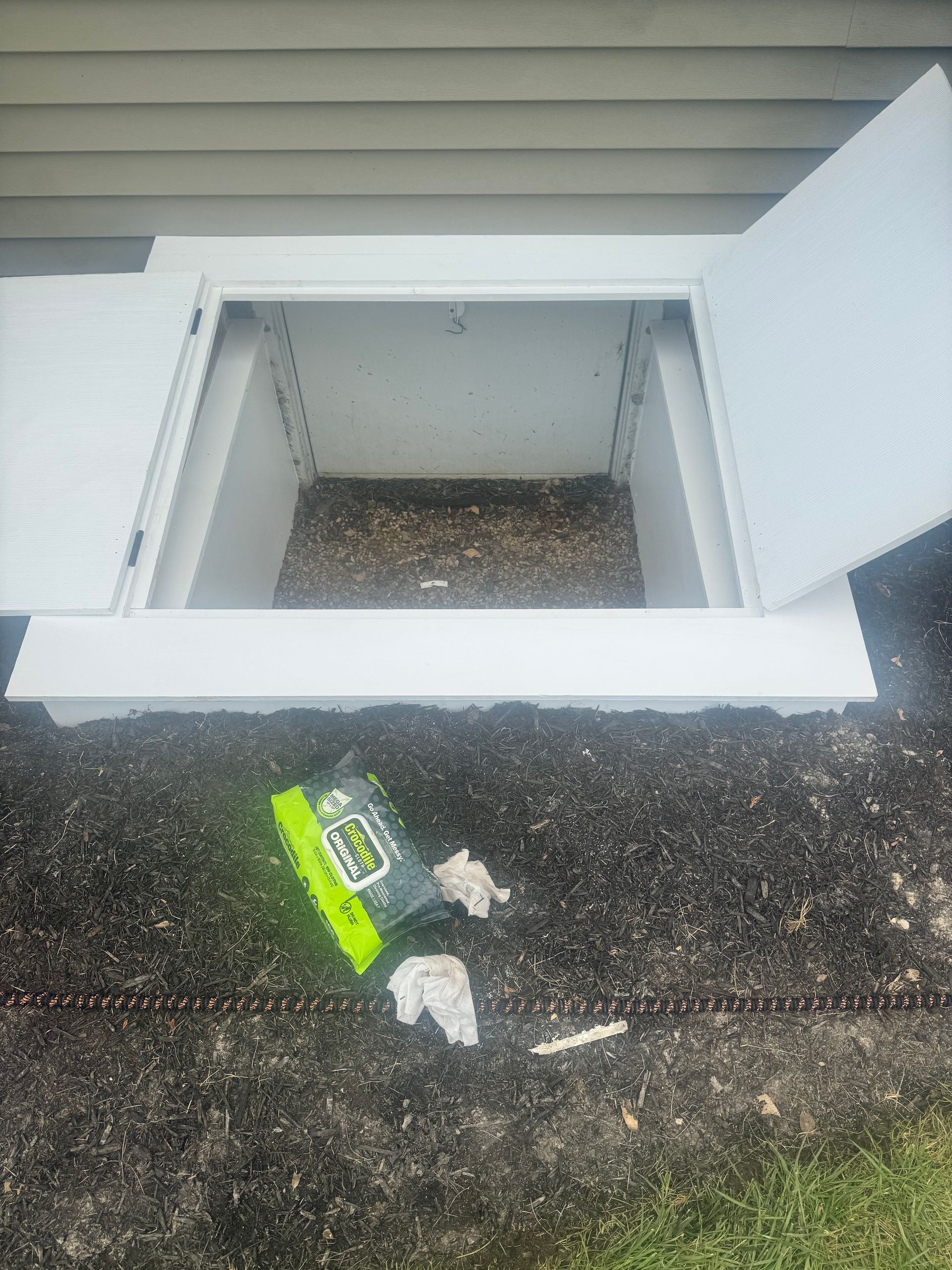 Open white basement window with a green snack wrapper on the ground below