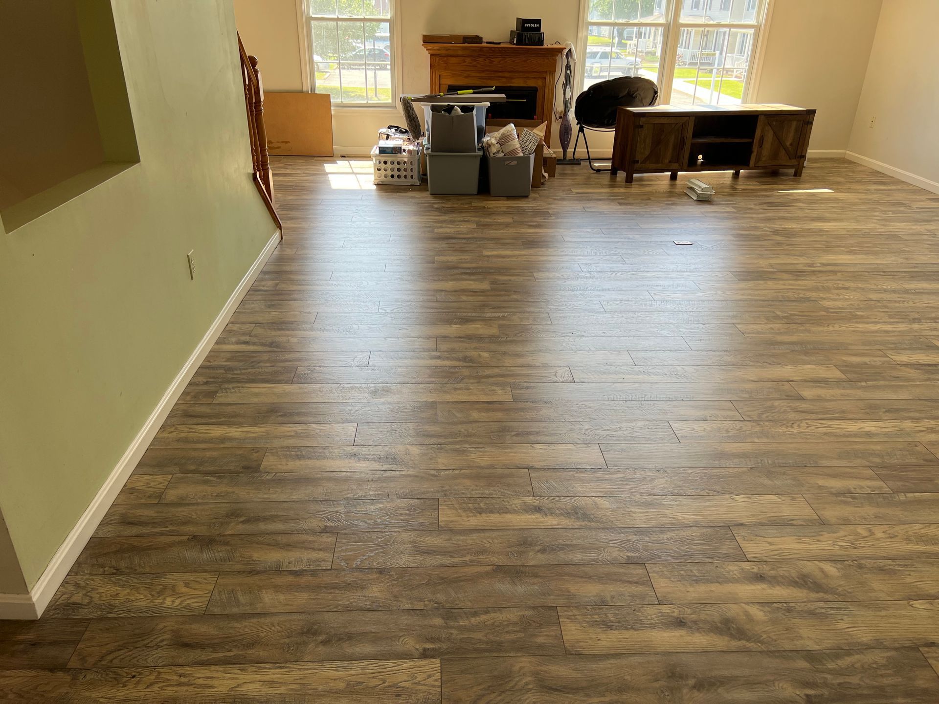 Empty room with wood-look flooring, pale green walls, and boxes near sunlit windows.
