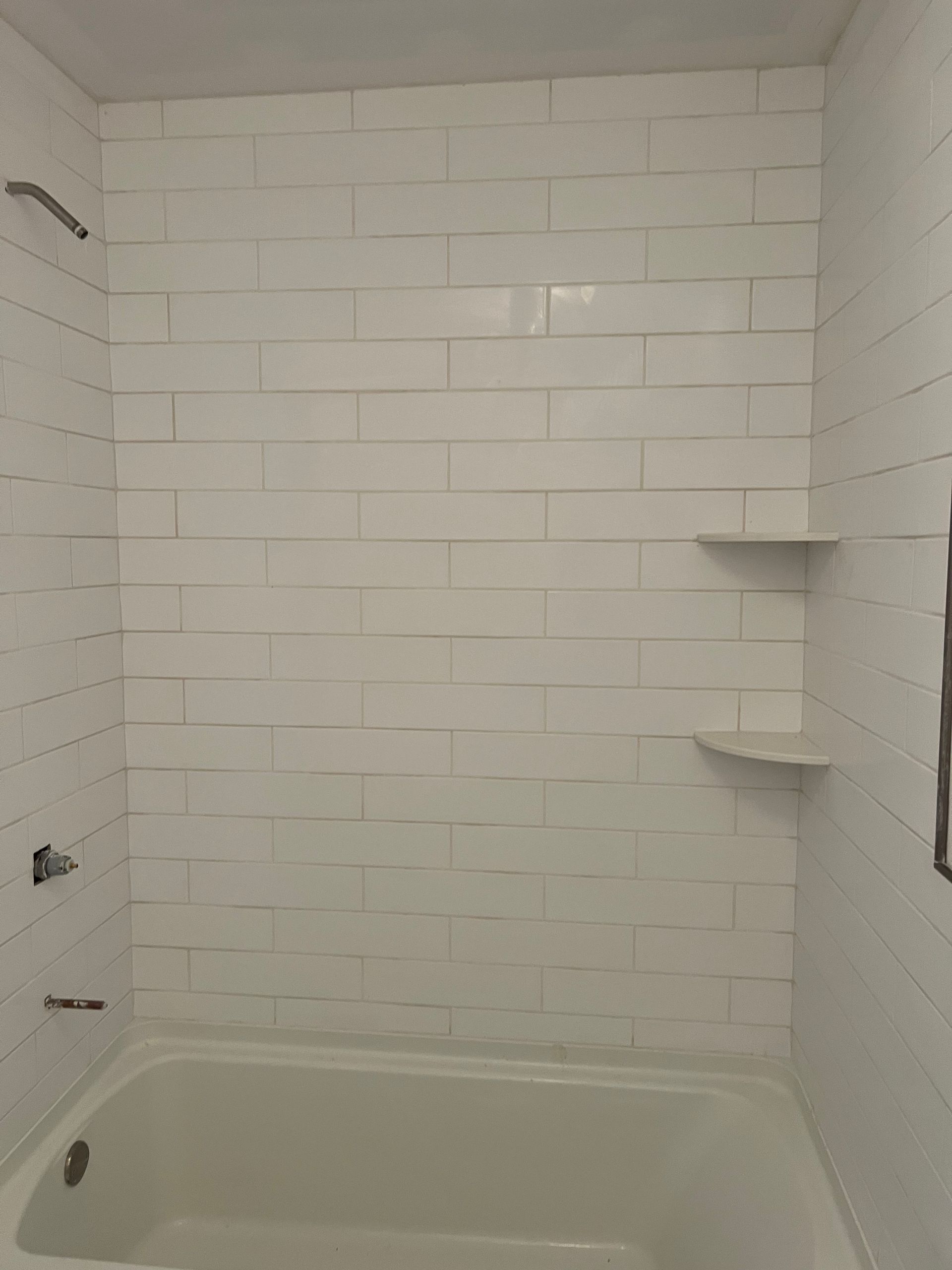 Small bathroom with a white-tiled shower/tub and built-in corner shelves.