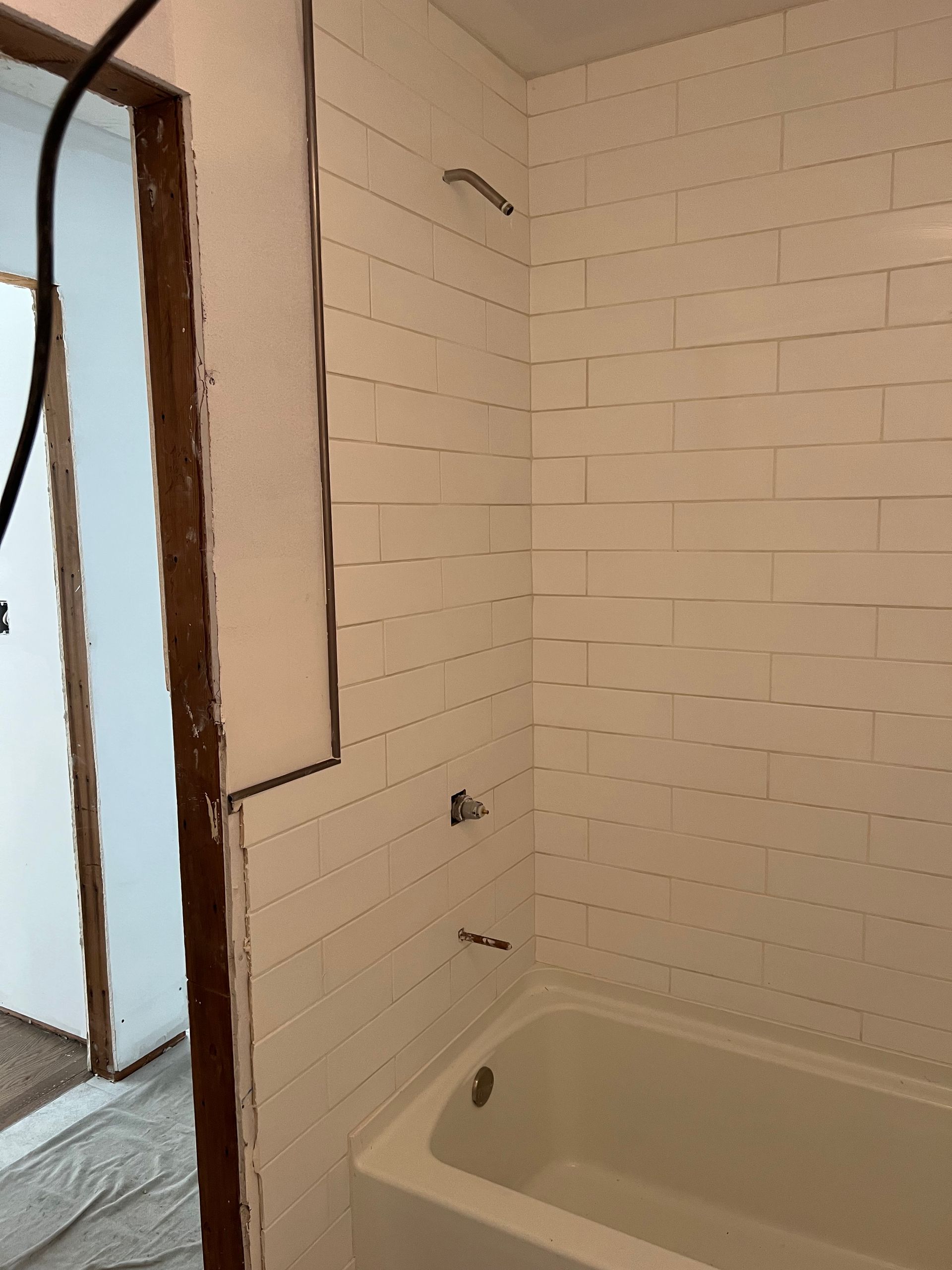 Small bathroom with a white bathtub, white tiled walls, and an unfinished doorway.