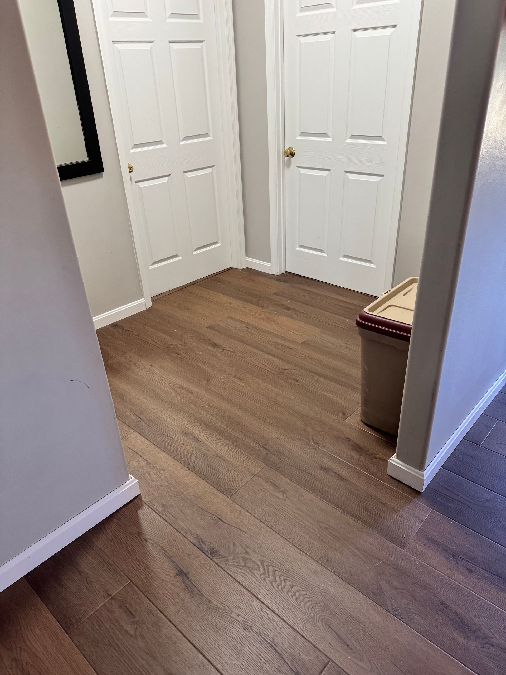 Hallway corner with white closet doors, wood flooring, and a small bench or storage ottoman