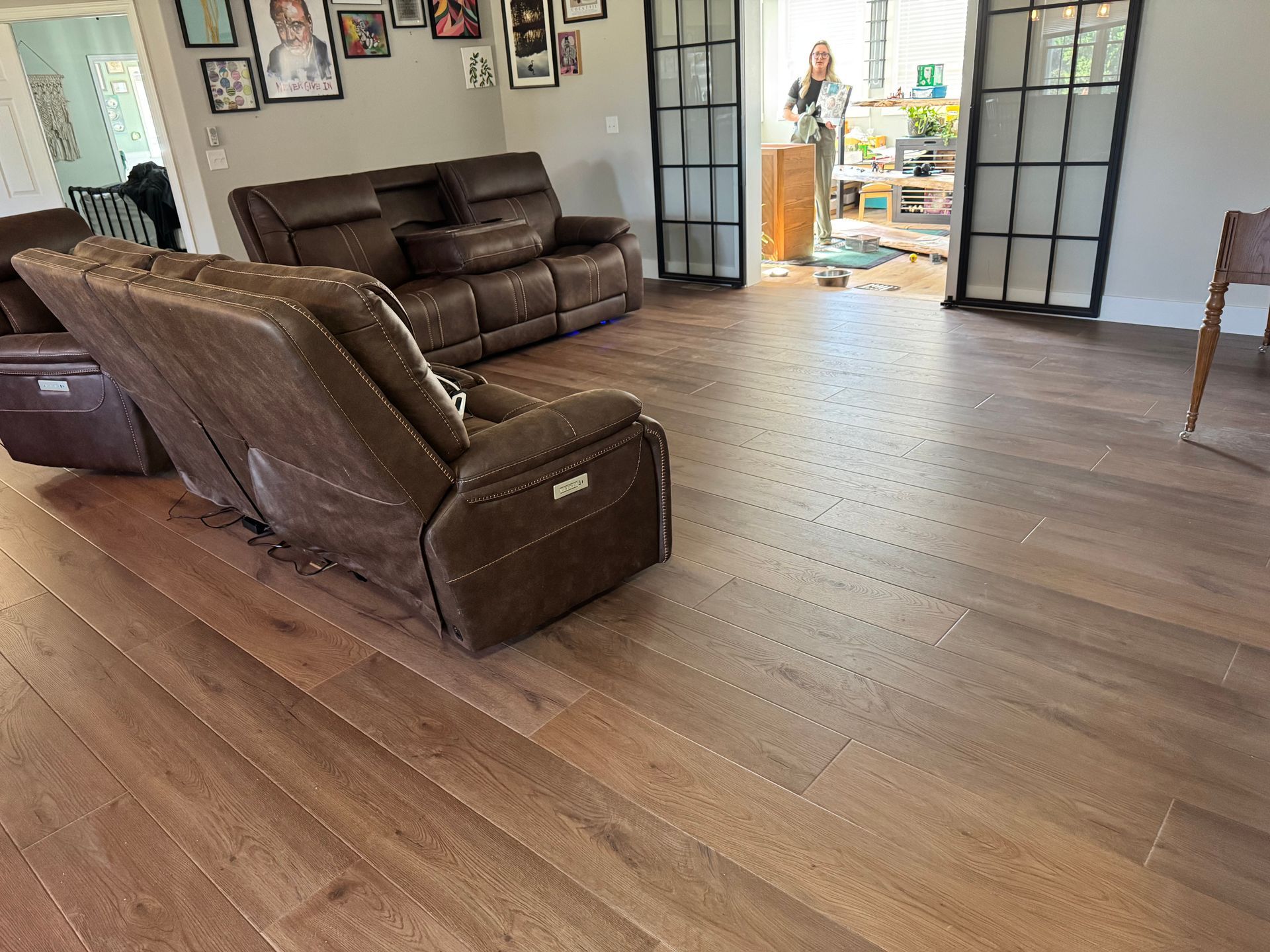 Living room with brown leather sofas, wood floors, and open double doors to a bright adjoining room