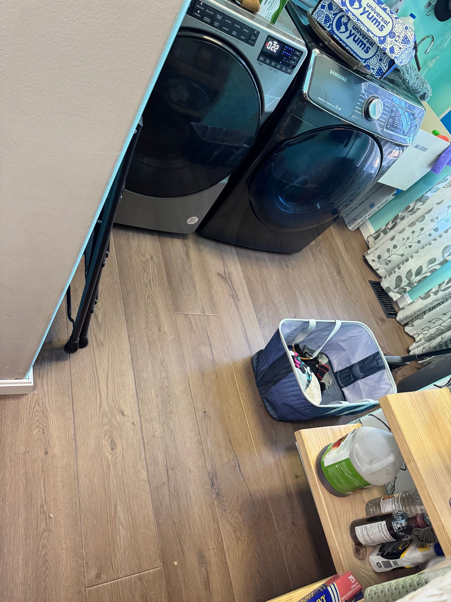 Laundry room with two front-loading washers, a hamper, and folded items on a shelf on the right.