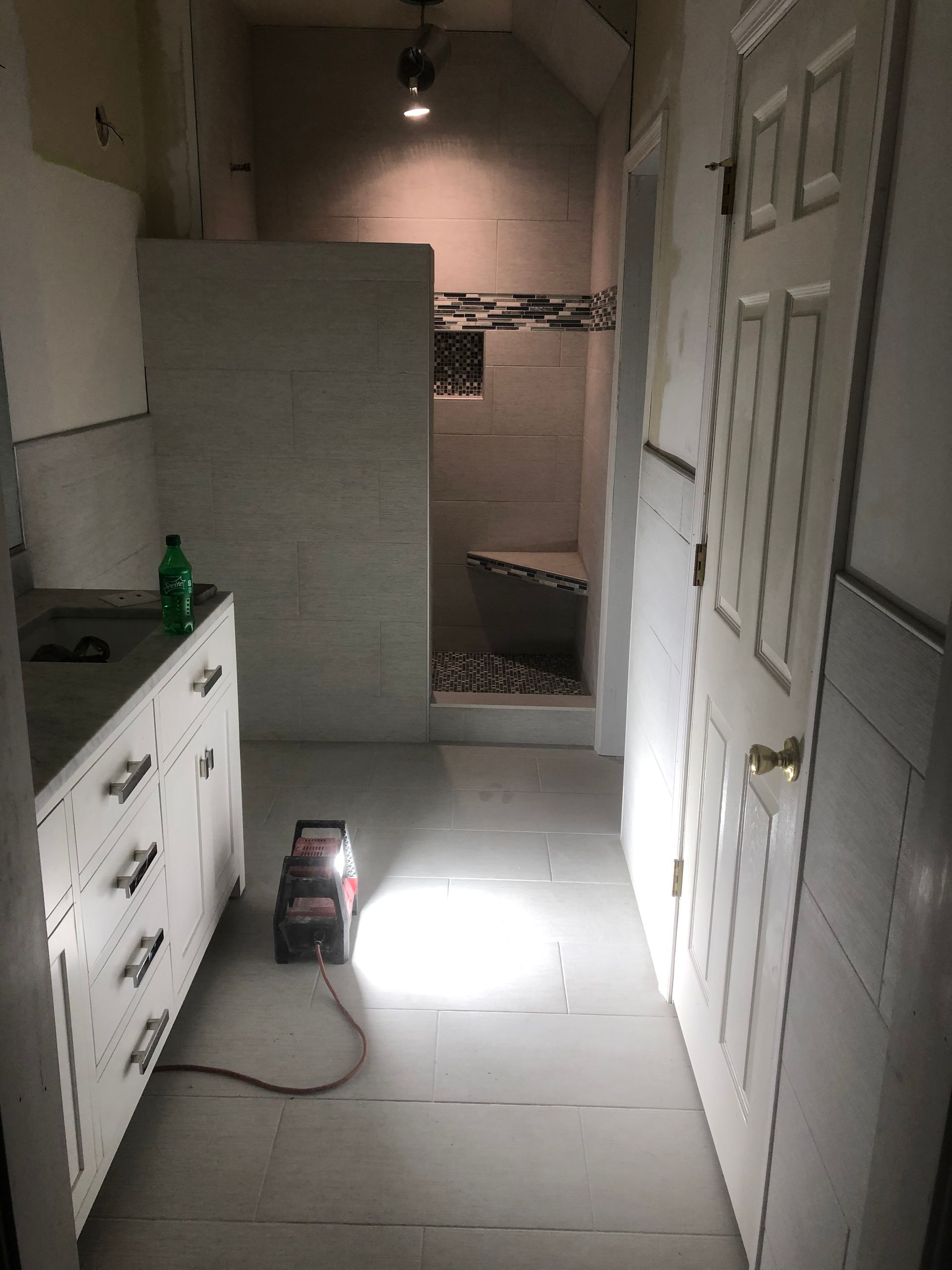 Dim hallway with white cabinets, doors, and a bright flashlight on the floor leading to a darker room.
