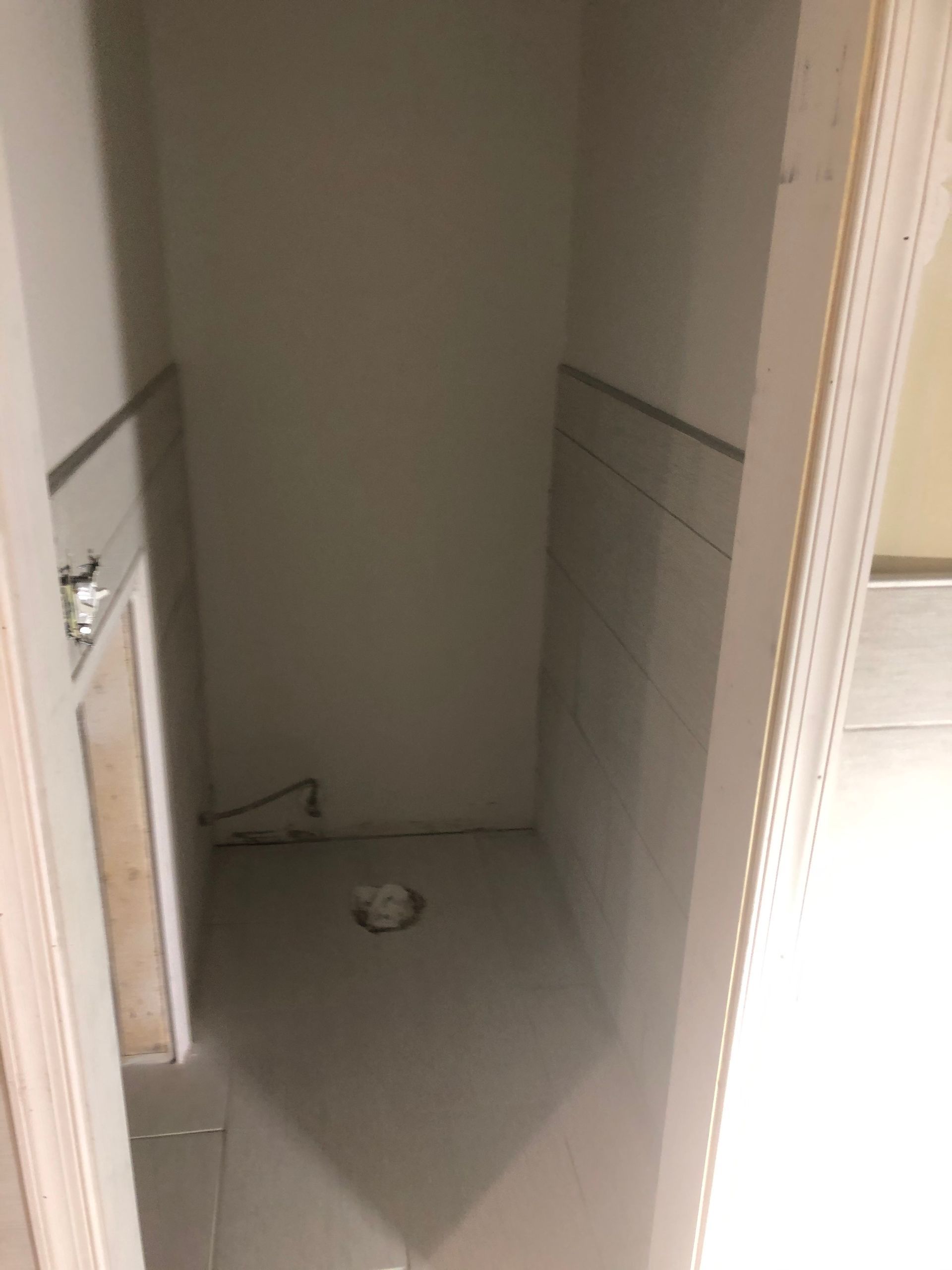 Narrow unfinished closet alcove with bare walls, floor, and a plumbing drain in the center.