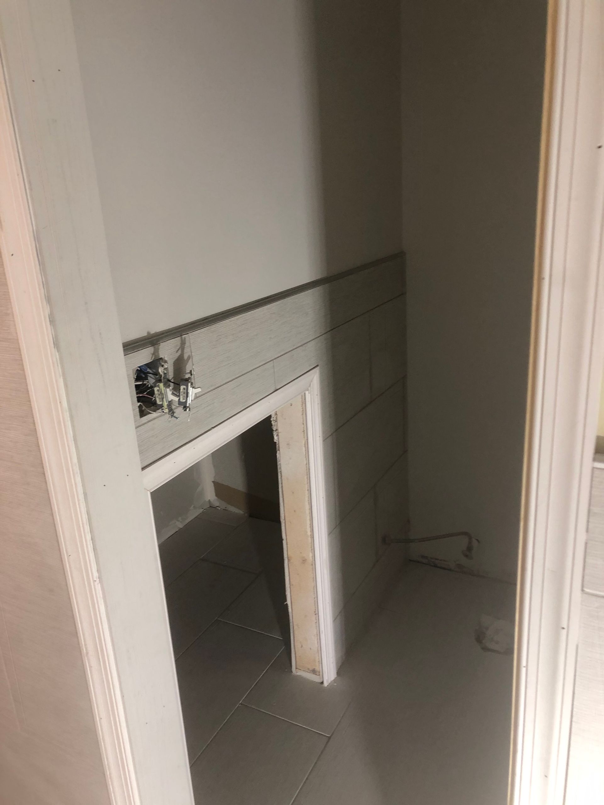 Narrow hallway with unfinished walls, tiled floor, and a small doorway opening into a dim room