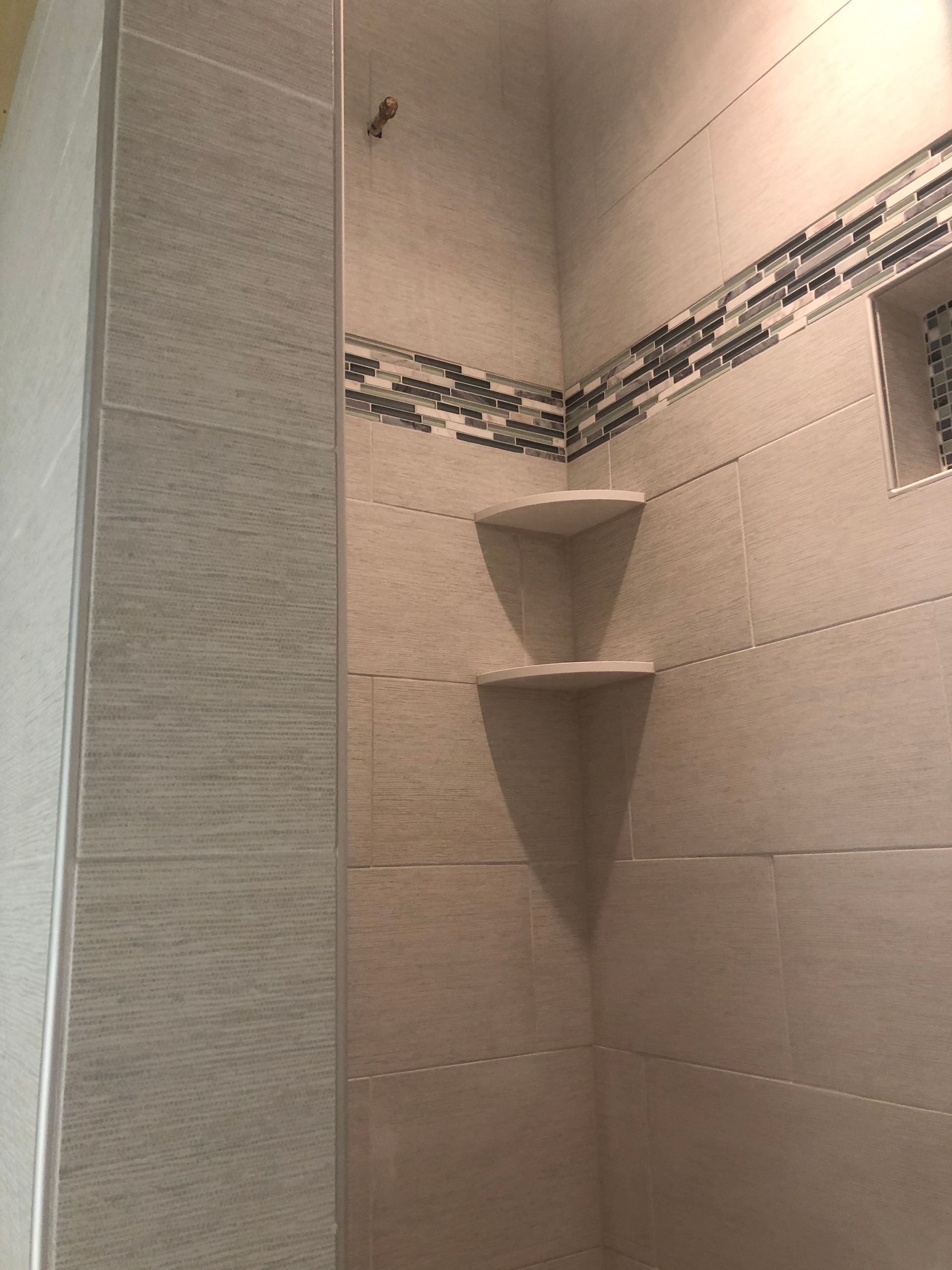 Corner shower with beige tile, decorative border, and two built-in corner shelves